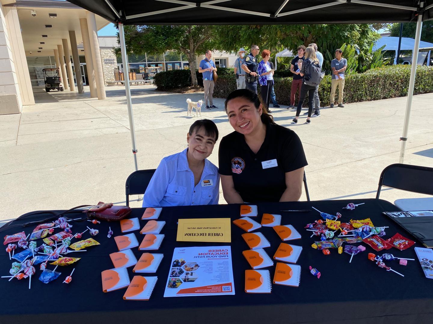 Career Education Table at Job Fair.  两位专业人士坐在桌边微笑着.